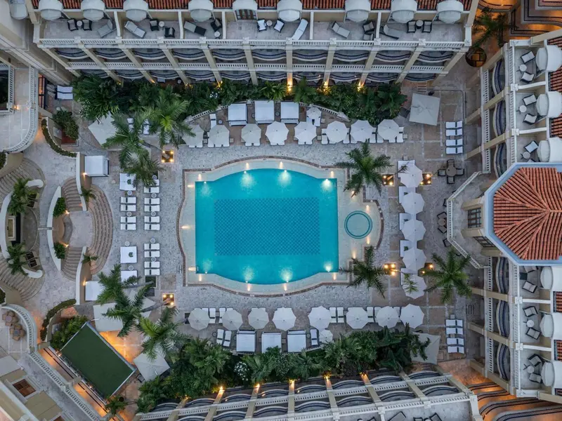 Vue aérienne d'une piscine entourée de transats et de palmiers dans un complexe hôtelier.