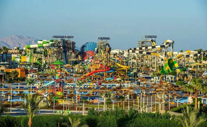 Un parc aquatique ensoleillé avec de nombreux toboggans colorés et des parasols.