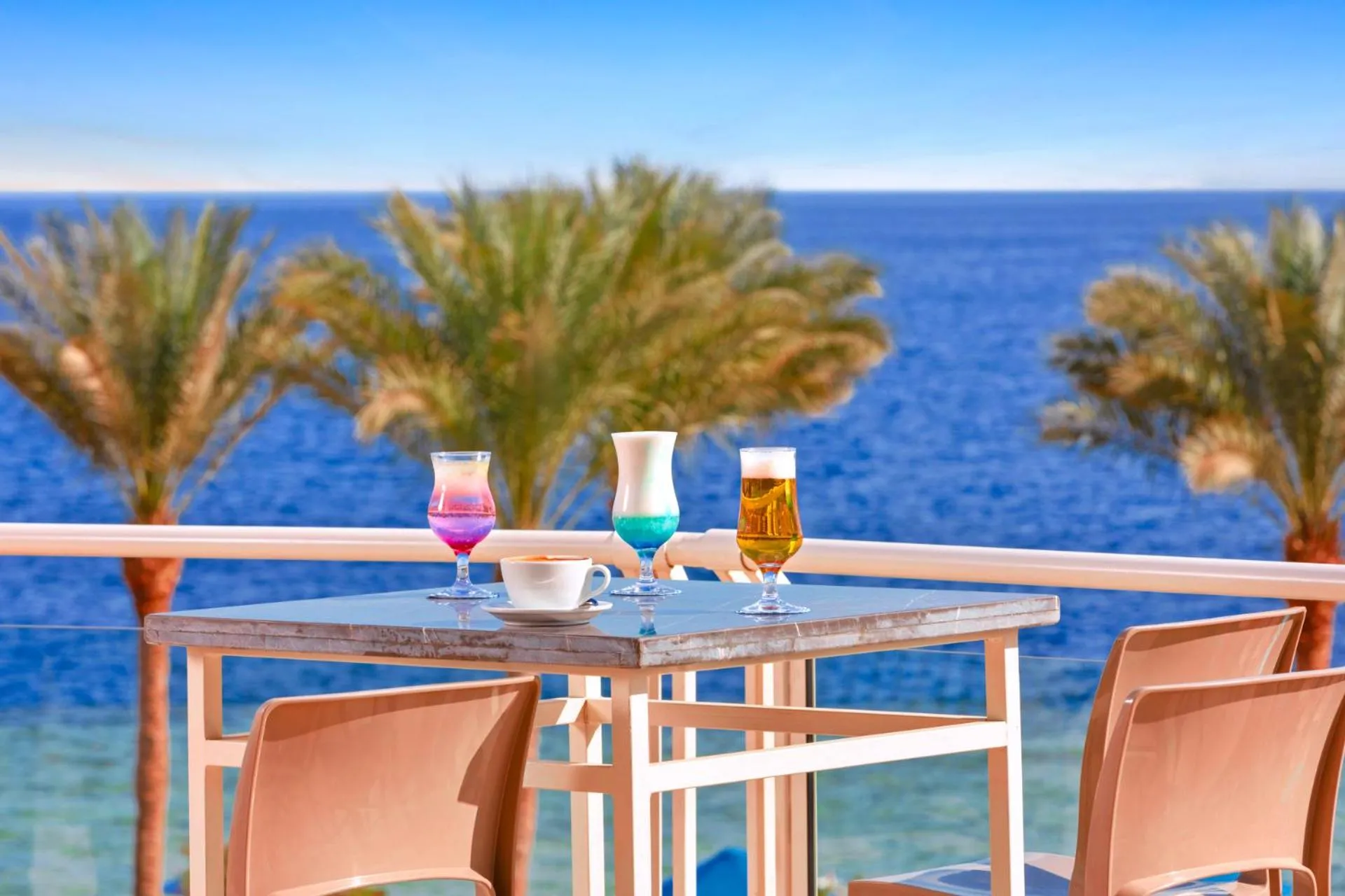 Une table avec des boissons et une tasse de café est mise en scène sur une terrasse avec vue sur la mer.