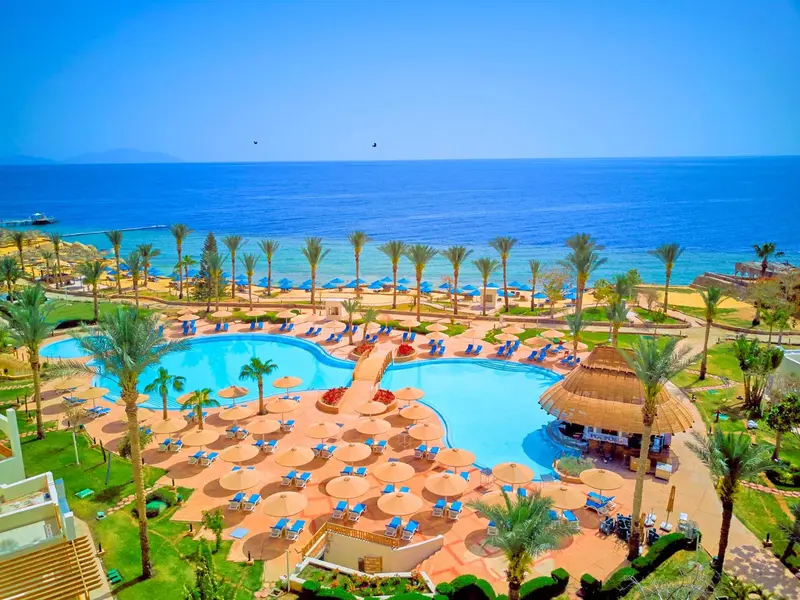 Vue aérienne d'un complexe hôtelier avec piscine et palmiers face à la mer.