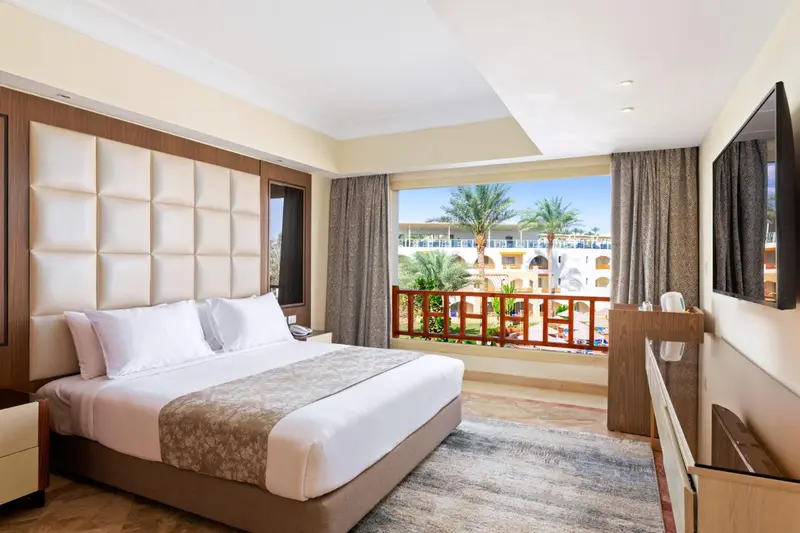 Chambre lumineuse avec un grand lit et vue sur une végétation luxuriante.