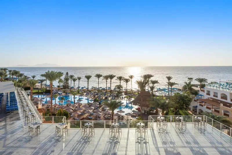 Terrasse avec tables et chaises donnant sur une piscine et la mer.