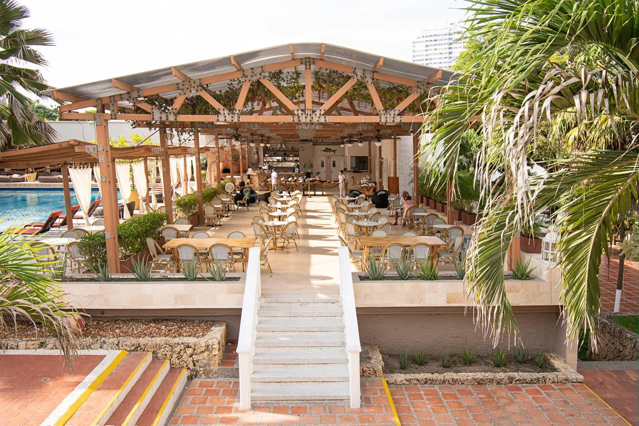 Terrasse ombragée avec tables et chaises près d'une piscine.
