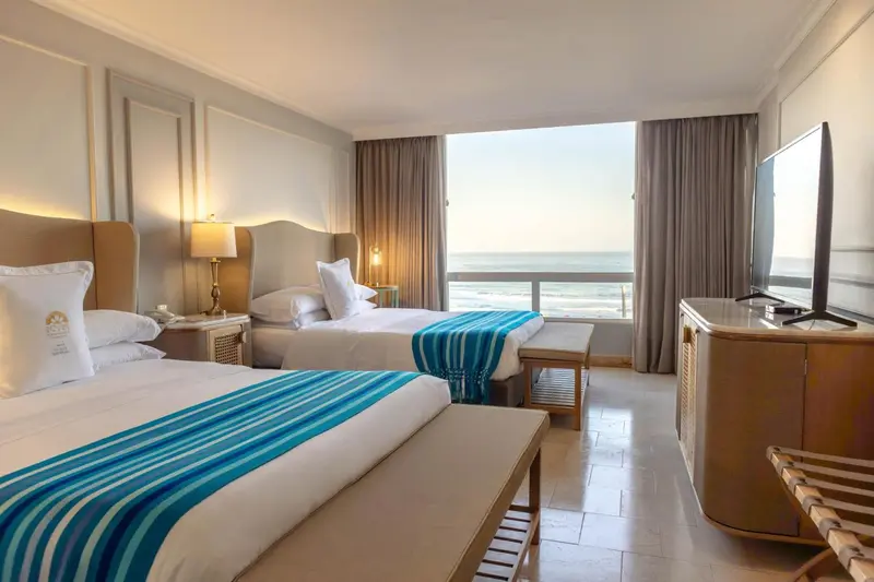 Chambre avec deux lits et vue sur la mer par une grande fenêtre.