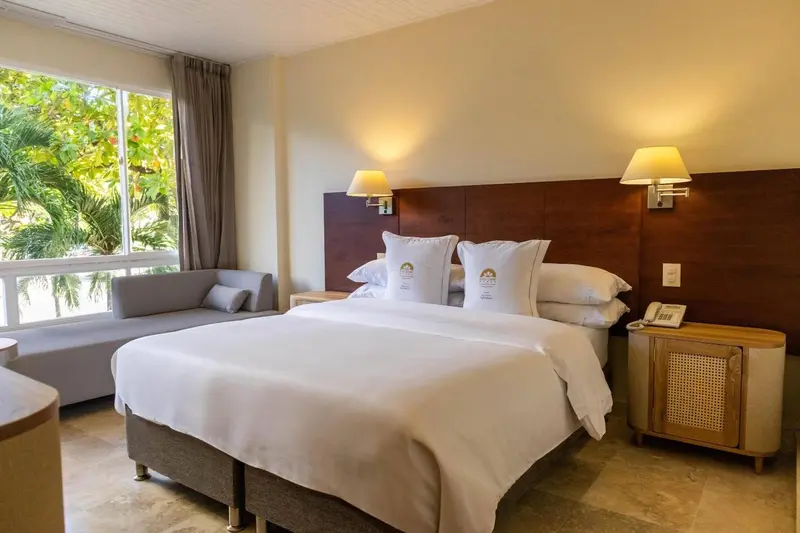 Une chambre lumineuse avec un grand lit et un coin salon près de la fenêtre.