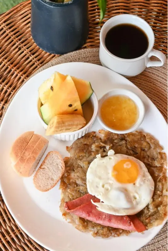 Petit-déjeuner copieux avec fruits, confiture, œuf au plat et jambon.