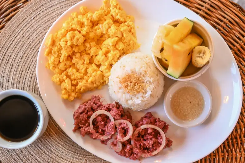 Assiette de nourriture avec des œufs brouillés, du riz, de la viande hachée et des fruits.