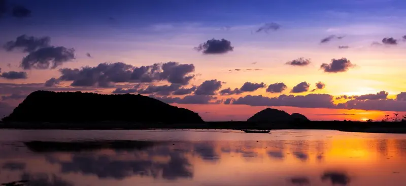 Ciel orangé et nuageux au coucher du soleil sur une mer calme.