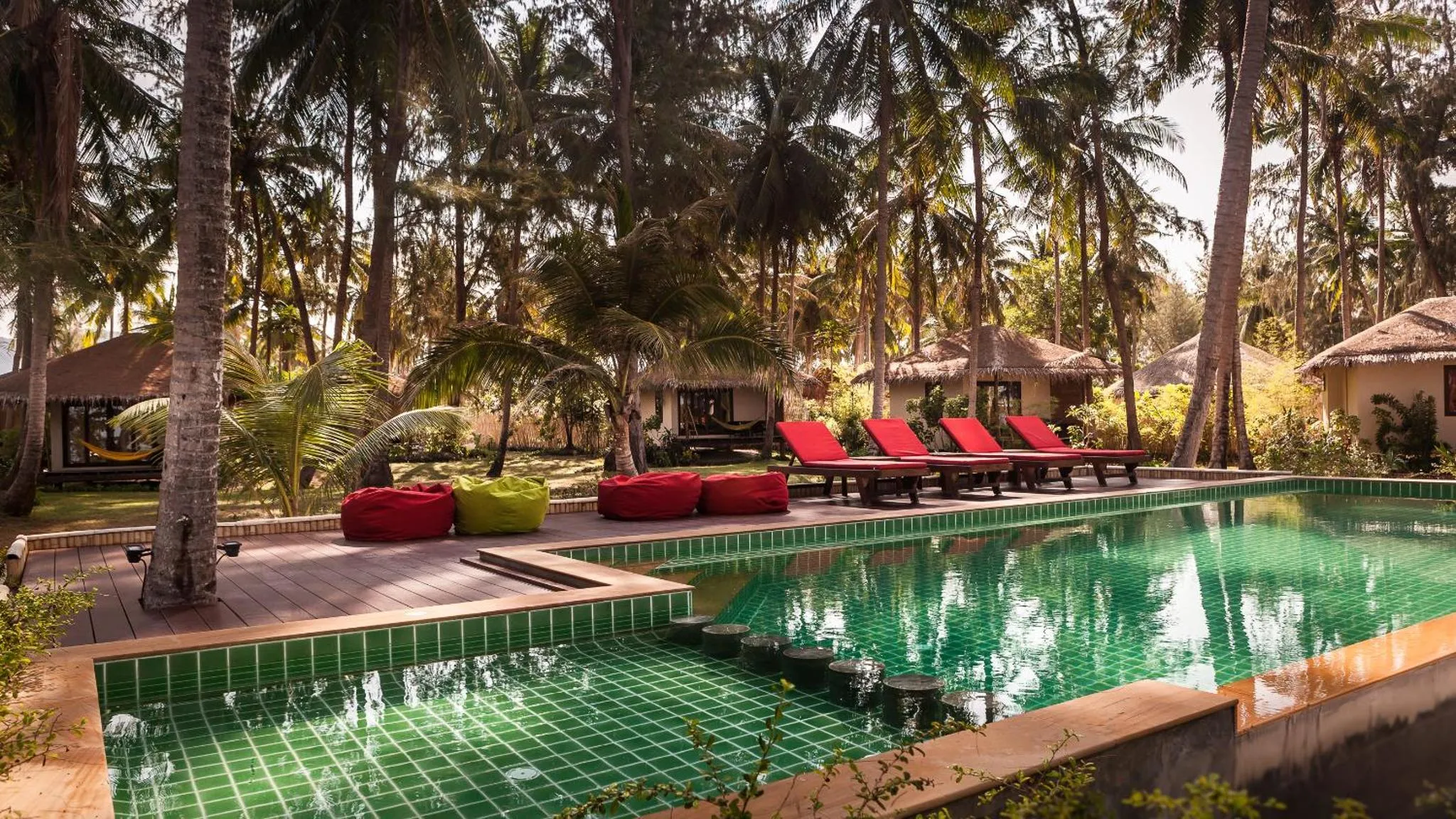 Transats rouges alignés au bord d'une piscine turquoise dans un jardin tropical.