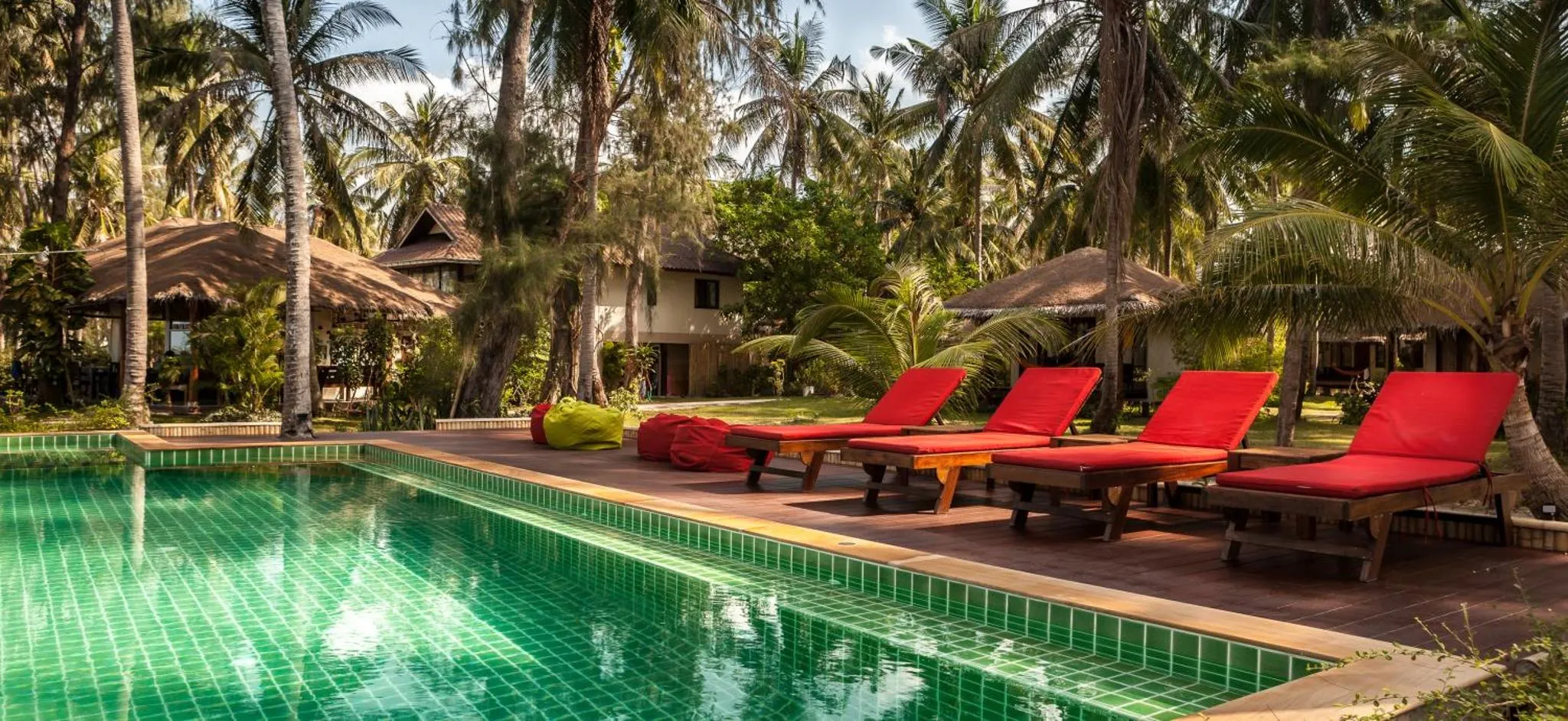 Transats rouges alignés au bord d'une piscine turquoise dans un jardin tropical.