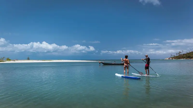 Deux personnes pratiquent le paddleboard dans une eau turquoise et peu profonde.