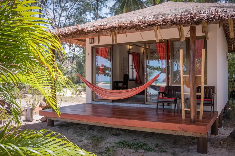 Une terrasse en bois abrite un hamac et du mobilier de jardin devant une habitation.