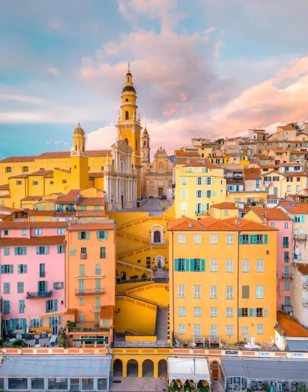 Vue d'ensemble d'une ville colorée avec une église au premier plan et un ciel nuageux au coucher du soleil.
