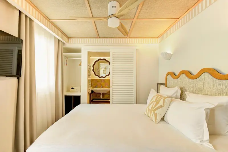 Une chambre lumineuse avec un lit fait et un espace lavabo visible.