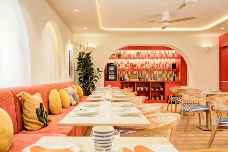 Une salle de restaurant lumineuse avec des tables dressées et des banquettes colorées.