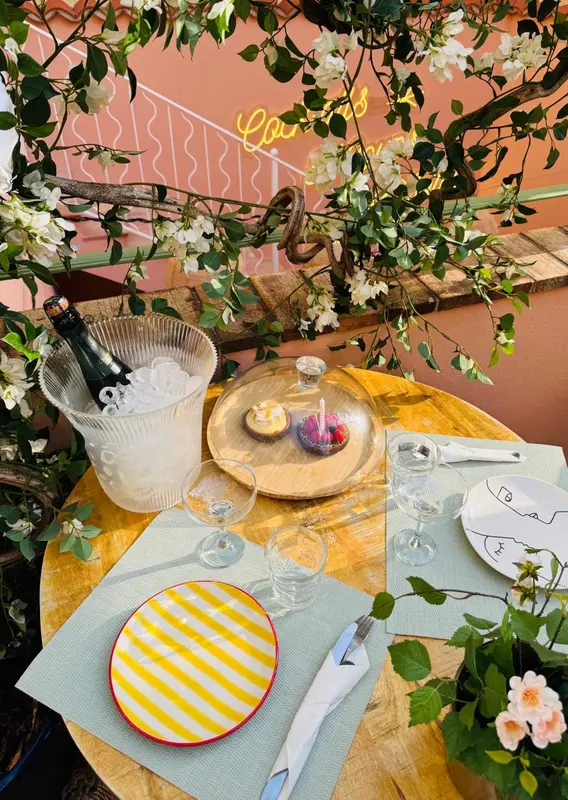 Une table dressée avec des verres, une bouteille et des assiettes sur une terrasse ensoleillée.