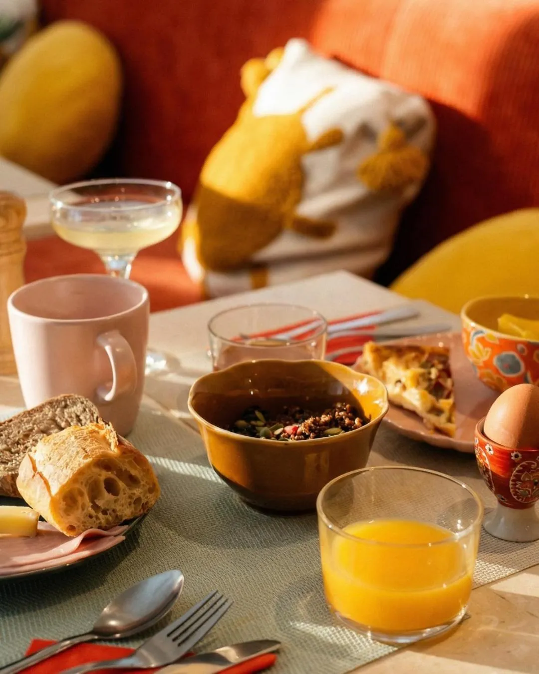 Une table est dressée pour le petit-déjeuner avec des viennoiseries, des fruits et des boissons.