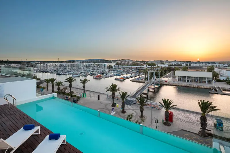 Terrasse avec piscine et vue sur un port au coucher du soleil.