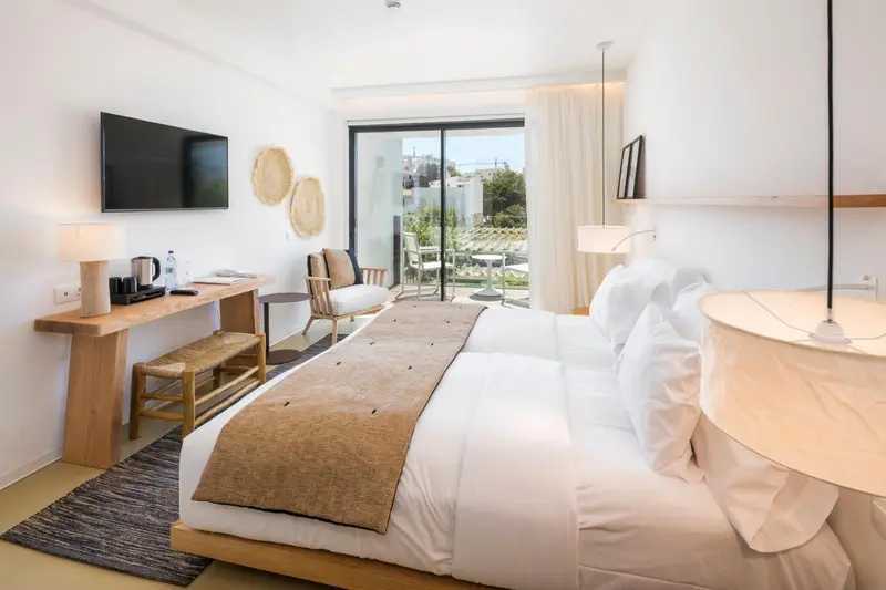 Chambre lumineuse avec un grand lit et un accès à une terrasse.