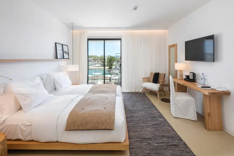Chambre lumineuse avec un grand lit et une vue sur un port de plaisance.