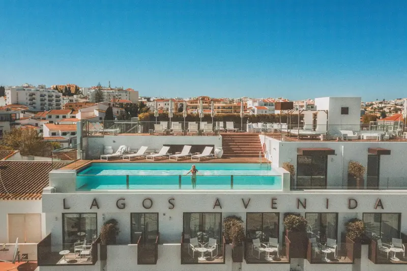 Vue aérienne d'une piscine rectangulaire entourée d'une terrasse avec des transats et des plantes.