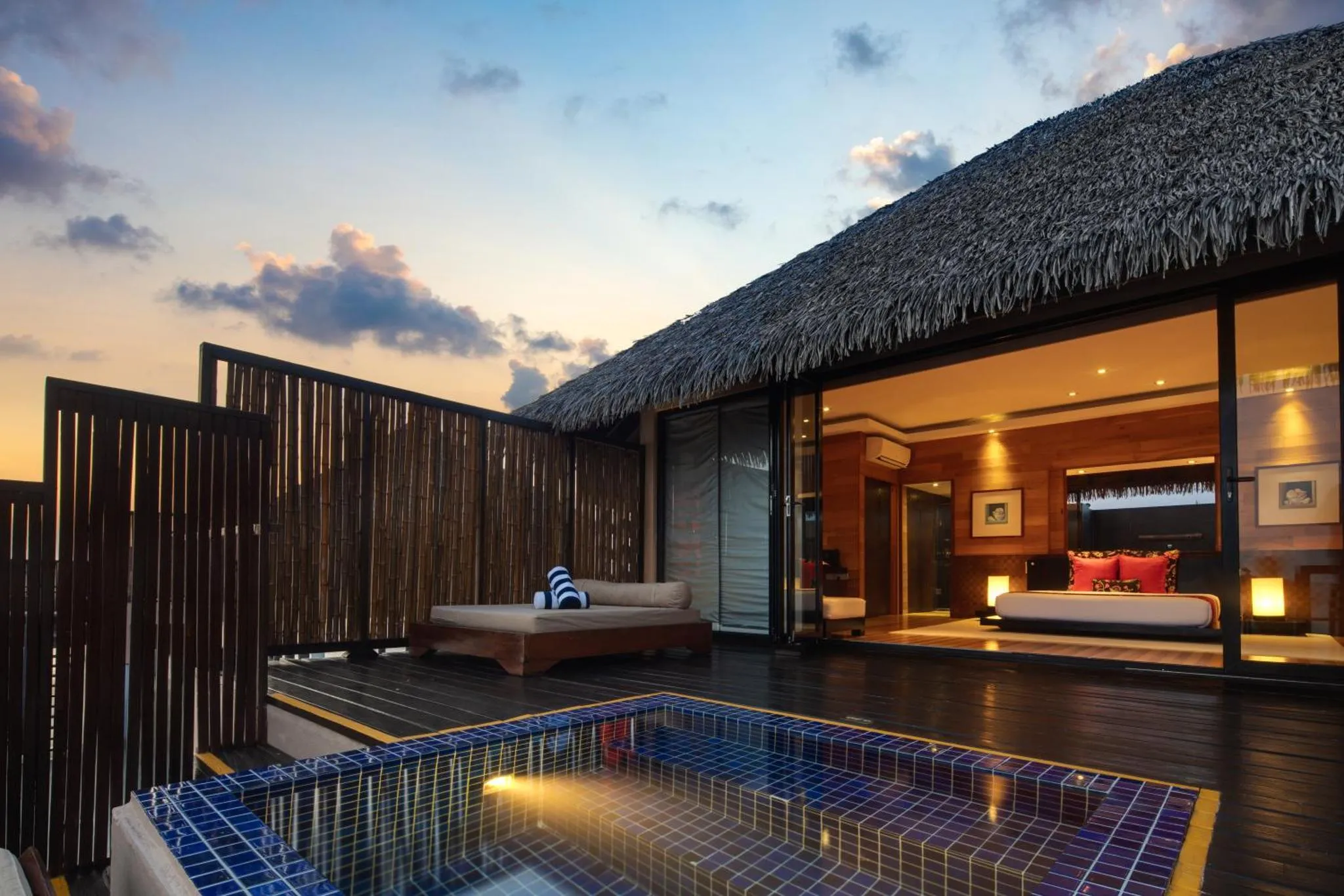 Terrasse en bois avec jacuzzi et lit de repos face à la mer.