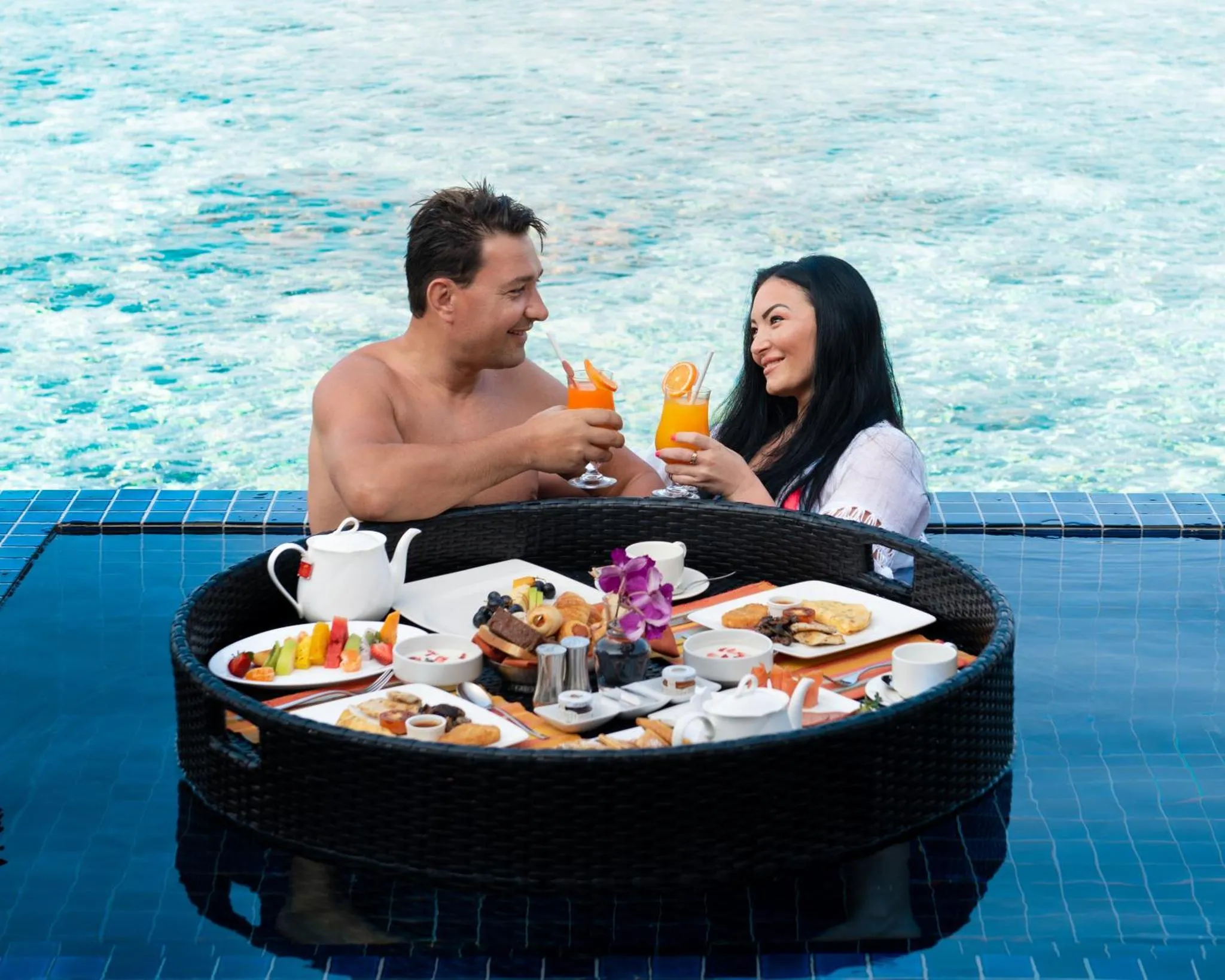 Un couple déguste des cocktails et un repas flottant dans une piscine.