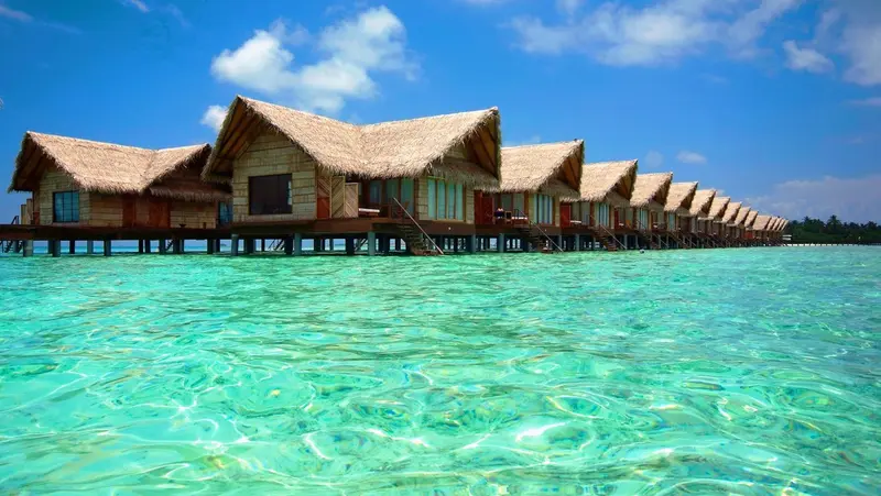 Bungalows sur pilotis au-dessus d'une eau turquoise et claire.