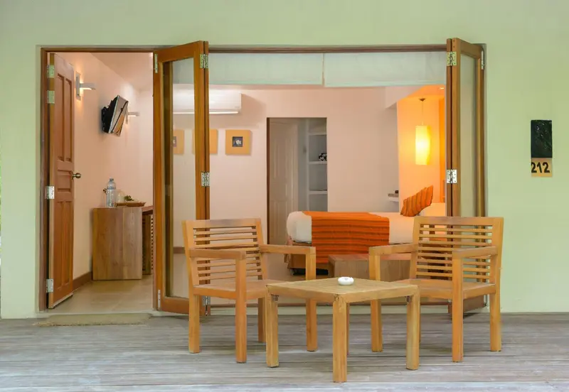 Une chambre lumineuse s'ouvre sur une terrasse en bois avec mobilier.