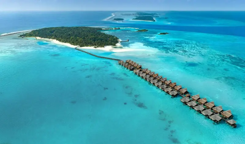 Vue aérienne d'un complexe hôtelier sur pilotis au milieu d'un lagon turquoise.