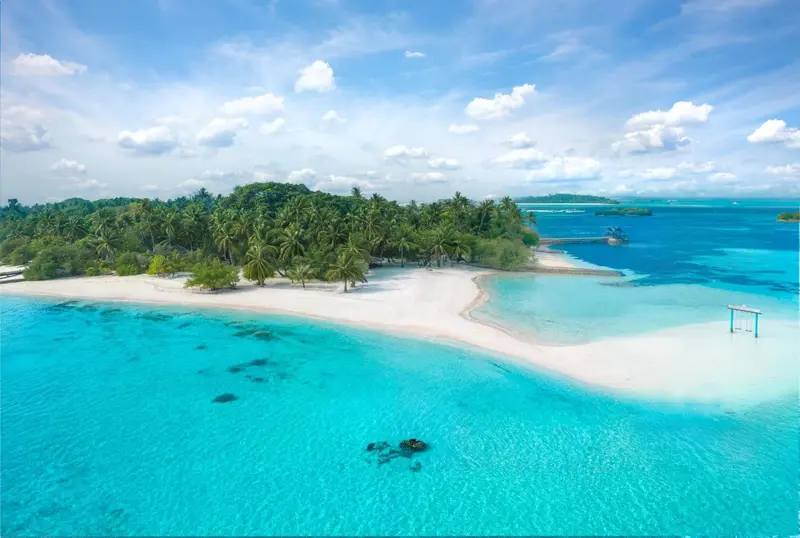 Vue aérienne d'une île tropicale bordée d'une plage de sable blanc et d'une eau turquoise.