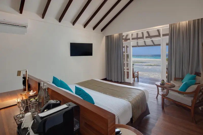 Une chambre lumineuse avec un lit double donnant sur une plage de sable blanc.