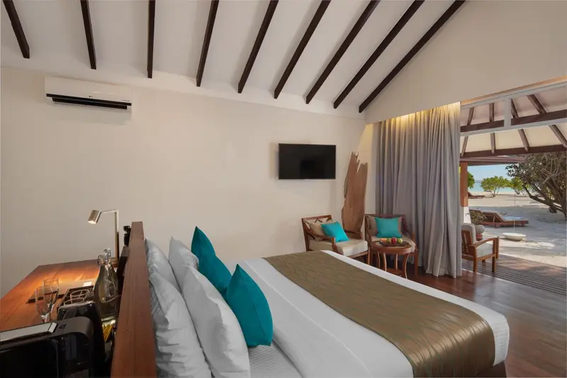 Une chambre lumineuse avec un lit double et un coin salon donnant sur une plage.