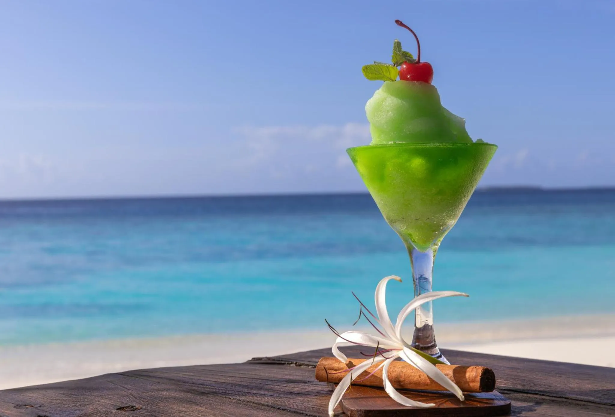 Boisson rafraîchissante sur une plage de sable blanc avec une mer turquoise en arrière-plan.