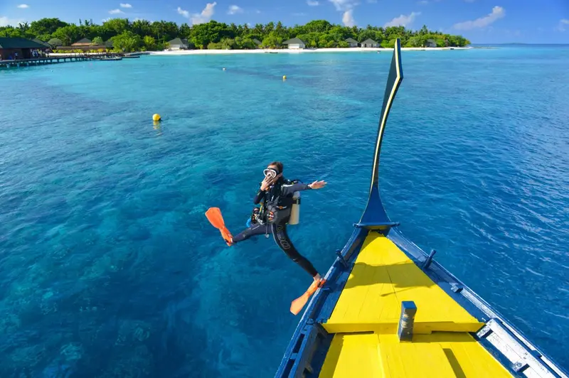 Une personne saute d'un bateau jaune dans une eau turquoise claire.