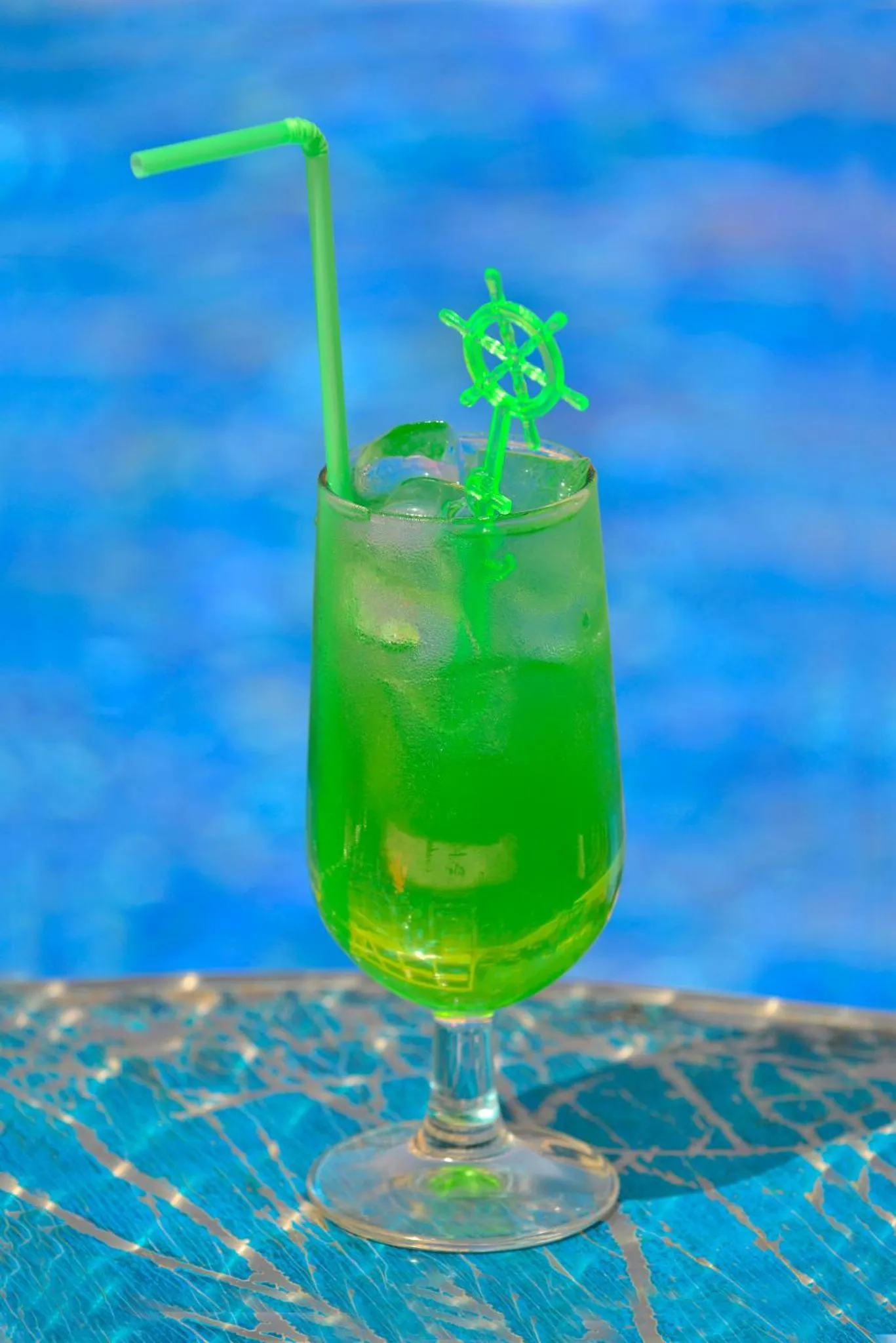 Un cocktail vert glacé est servi dans un verre haut au bord d'une piscine.