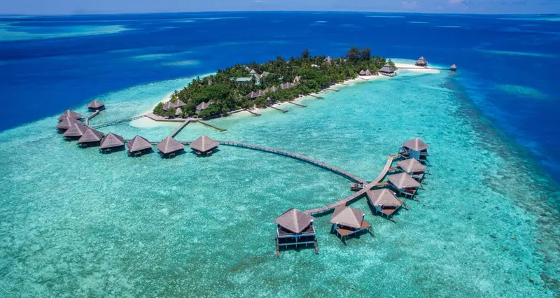 Vue aérienne d'une île tropicale avec des bungalows sur pilotis.