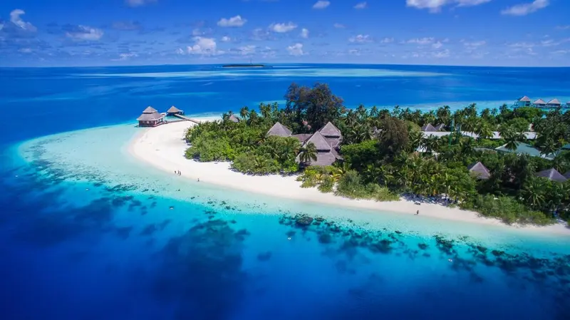 Vue aérienne d'une île tropicale avec des bungalows sur pilotis et une plage de sable blanc.