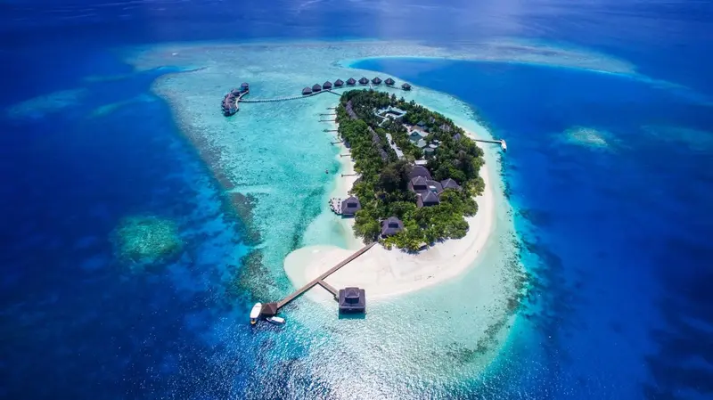 Vue aérienne d'une île tropicale avec des bungalows sur pilotis et une plage de sable blanc.
