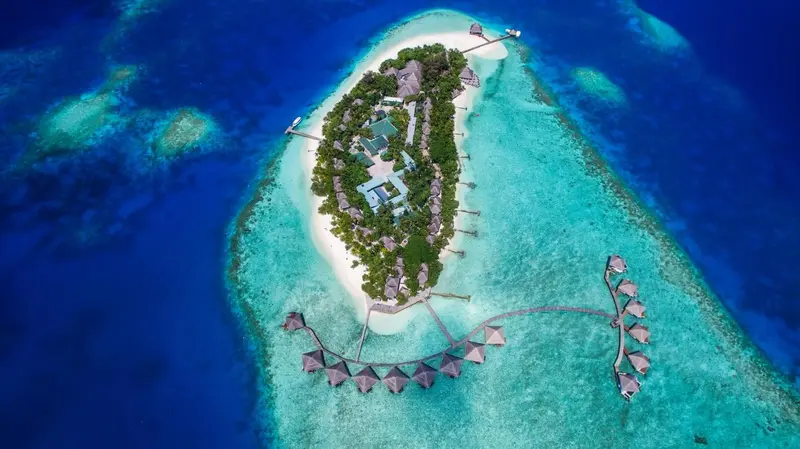 Vue aérienne d'une île tropicale entourée d'eaux turquoise et de bungalows sur pilotis.
