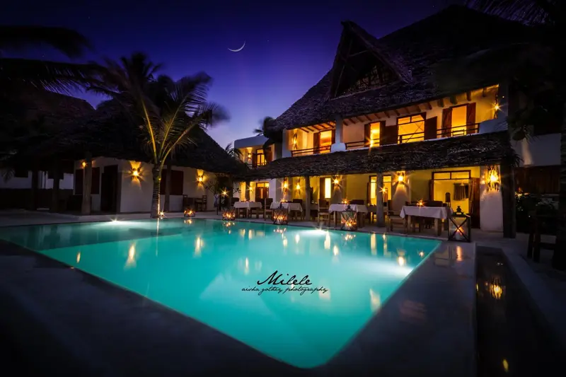 Bâtiment éclairé avec piscine au premier plan sous un ciel nocturne.
