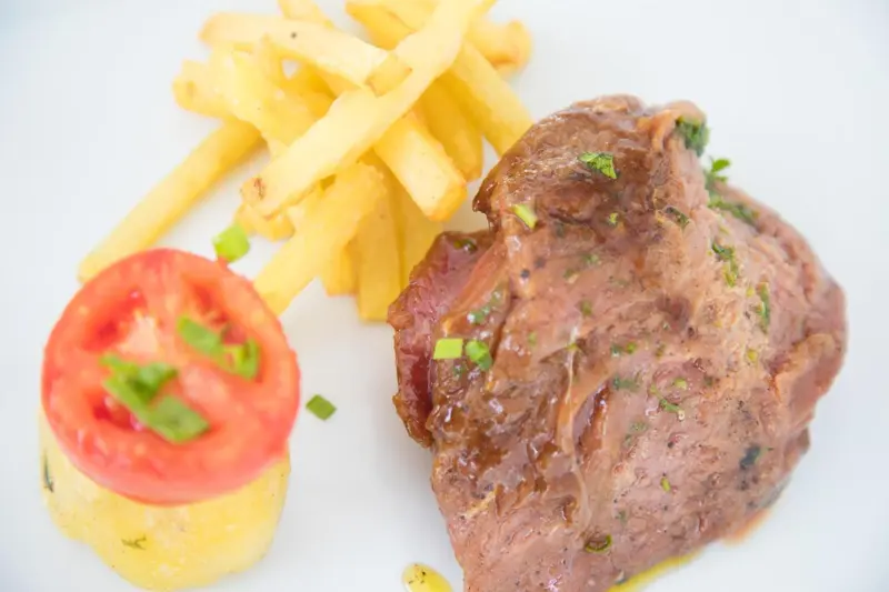 Assiette de viande accompagnée de frites et d'une tomate.