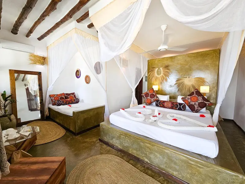 Chambre lumineuse avec lits décorés de fleurs et moustiquaires.