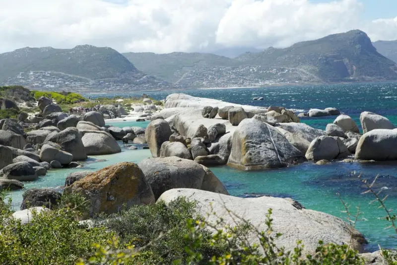 Côte rocheuse avec végétation et vue sur la mer et les montagnes.