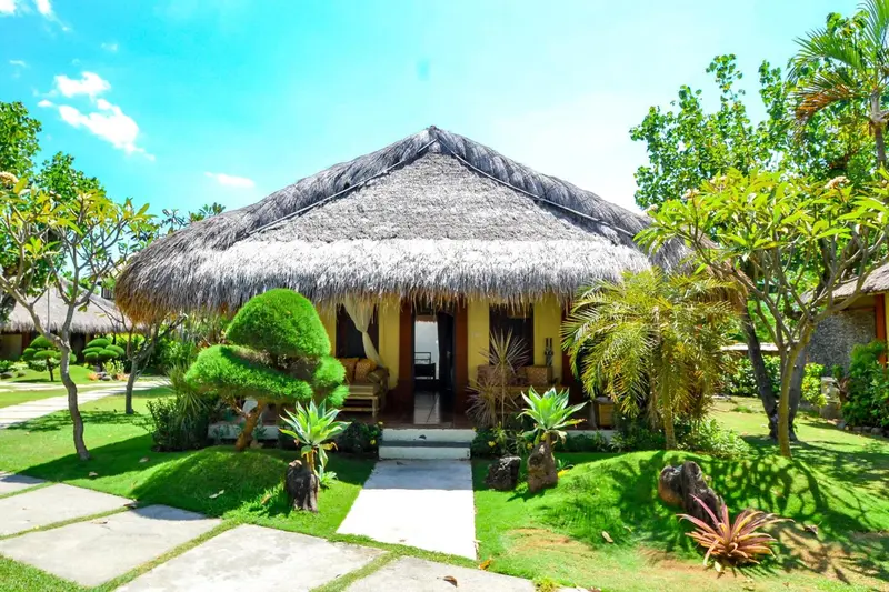 Une petite maison de style tropical avec un toit de chaume se trouve au milieu d'une végétation luxuriante.