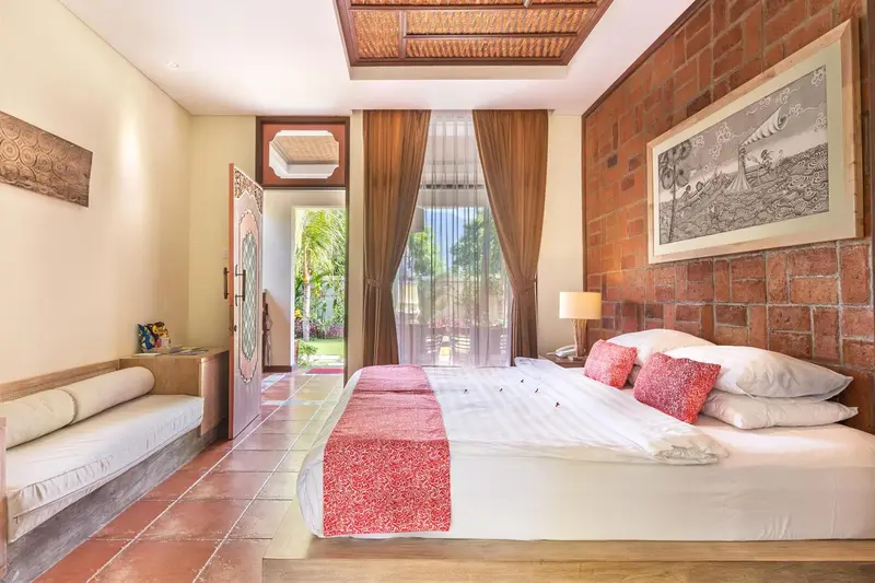 Une chambre lumineuse avec un lit recouvert d'une courtepointe rouge et un canapé en rotin.