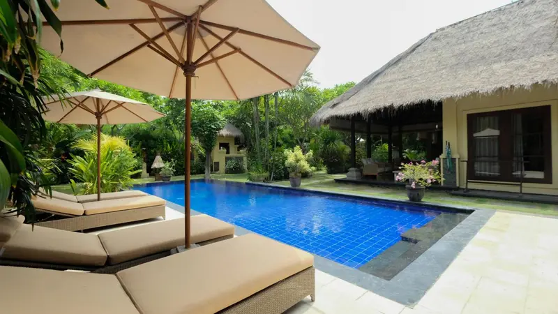 Transats et parasols bordent une piscine turquoise dans un jardin tropical.