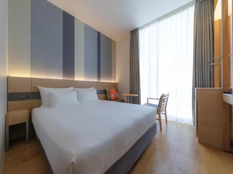 Chambre lumineuse avec un grand lit et une fenêtre drapée.