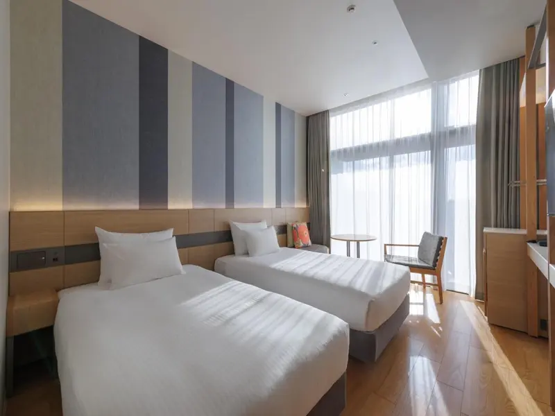 Chambre lumineuse avec deux lits simples et une grande fenêtre.