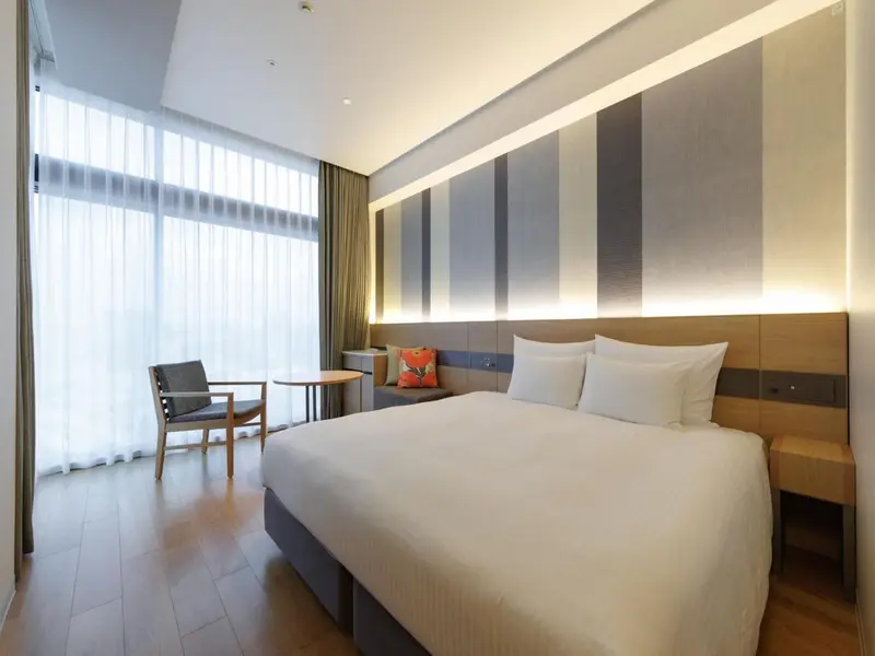 Une chambre lumineuse avec un grand lit et un fauteuil près de la fenêtre.